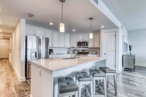 A modern kitchen with white cabinets, stainless steel appliances, a large island with bar stools, and pendant lighting. - Blu 101 - Luxurious first-floor condo with hot tub, heated outdoor pool - near entertainment (Fort Walton Beach)