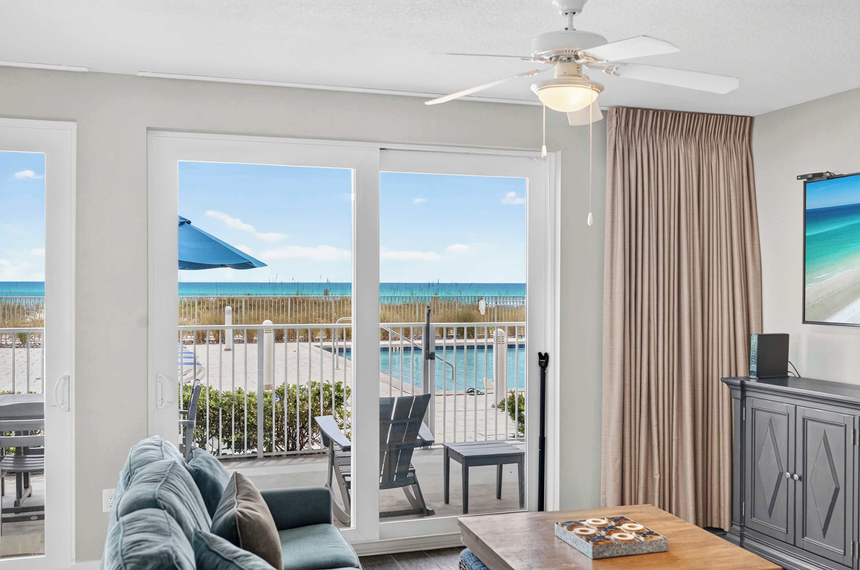 A room with a view of a pool and beach, a ceiling fan, and a dining area with a table and chairs.