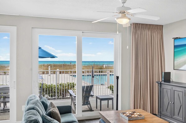 A room with a view of a pool and beach, a ceiling fan, and a dining area with a table and chairs. - Blu 101 - Luxurious first-floor condo with hot tub, heated outdoor pool - near entertainment (Fort Walton Beach)