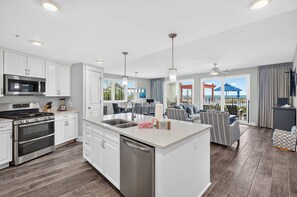 A modern kitchen with a central island, stainless steel appliances, and a dining area with a view. - Blu 101 - Luxurious first-floor condo with hot tub, heated outdoor pool - near entertainment (Fort Walton Beach)