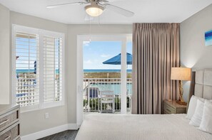 A hotel room with a bed, a nightstand, a lamp, a ceiling fan, and a view of the ocean through a balcony door. - Blu 101 - Luxurious first-floor condo with hot tub, heated outdoor pool - near entertainment (Fort Walton Beach)