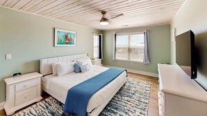 Un dormitorio con cama, mesitas de noche, televisor y ventilador de techo.