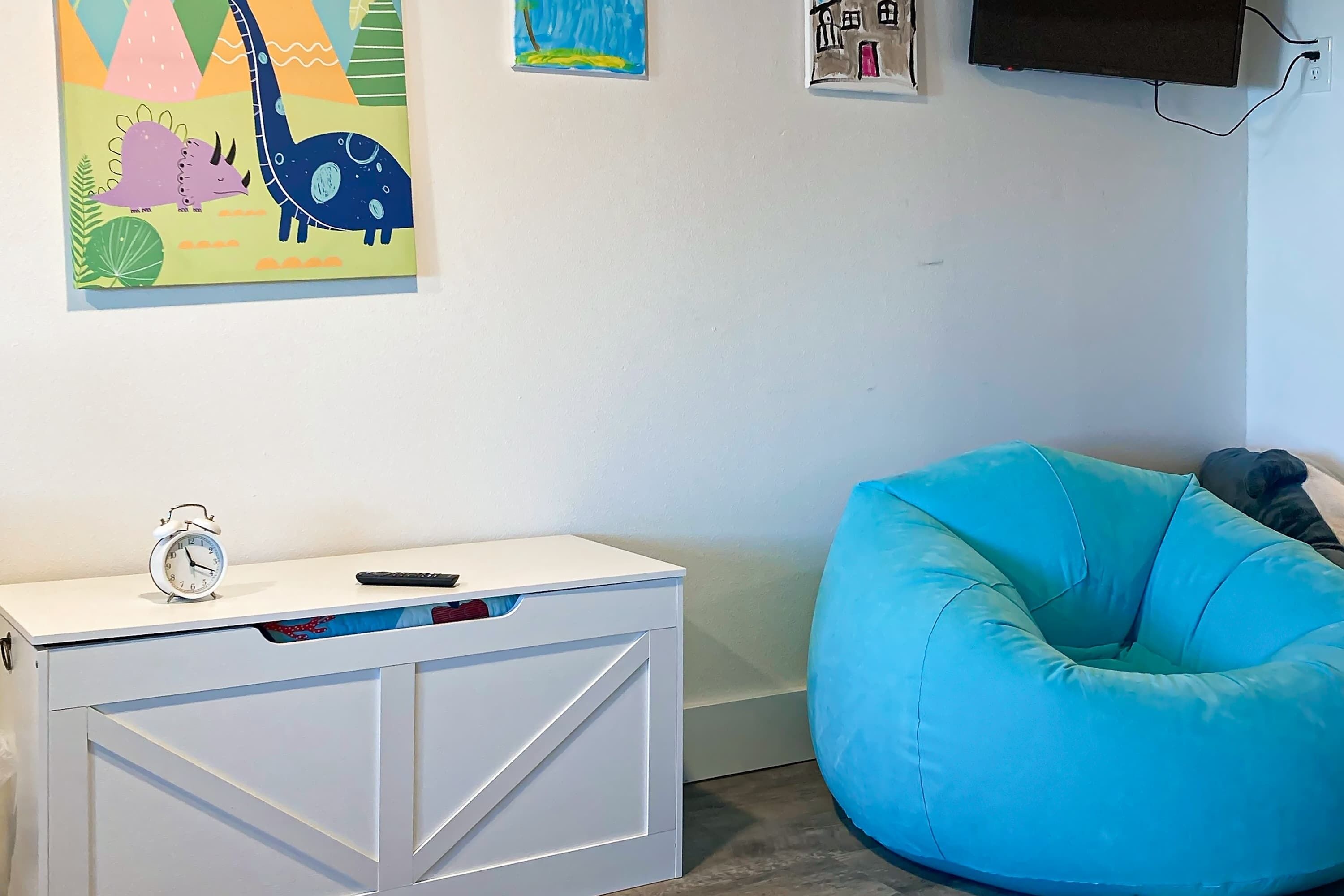 Habitació amb escriptori blanc, butaca de sacs blava i obra d'art colorida a la paret.