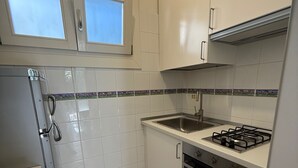 Eine kleine Küche mit weißen Schränken, einem Gasherd, einer Spüle und einem Kühlschrank.