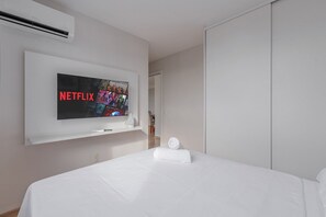 A hotel room with a flat-screen TV mounted on the wall displaying the Netflix logo, a neatly made bed with a rolled towel, and a white wardrobe. - Mirante #606 - Space and Comfort by Carpediem (Fortaleza)