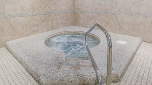 A stone hot tub with a metal ladder, surrounded by tiled walls. - 15th Floor Stunning Condo, Splash pad w multiple pools & hot tub (Destin)