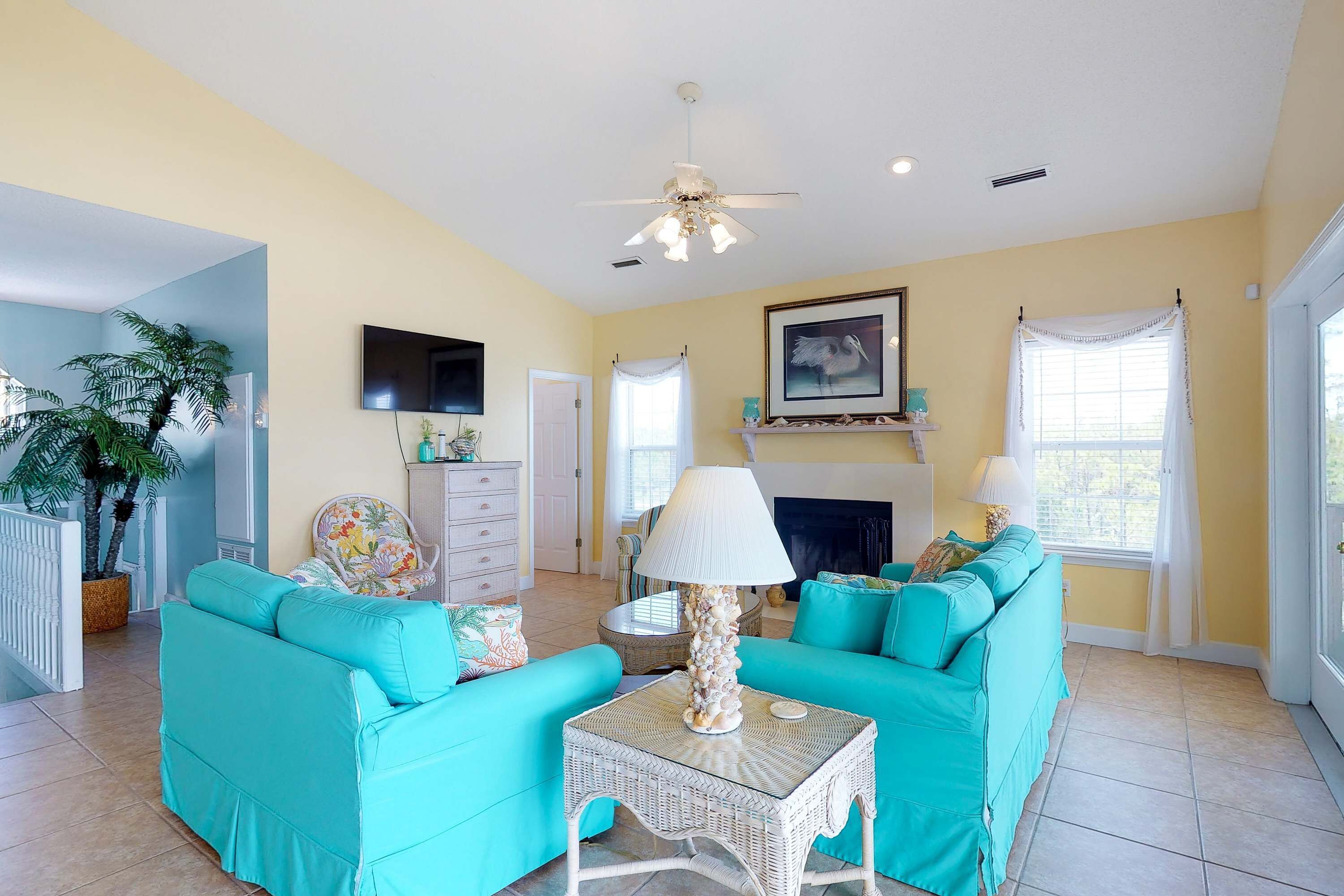 Un salon avec des canapés de couleur turquoise, une cheminée, un ventilateur de plafond et un téléviseur.