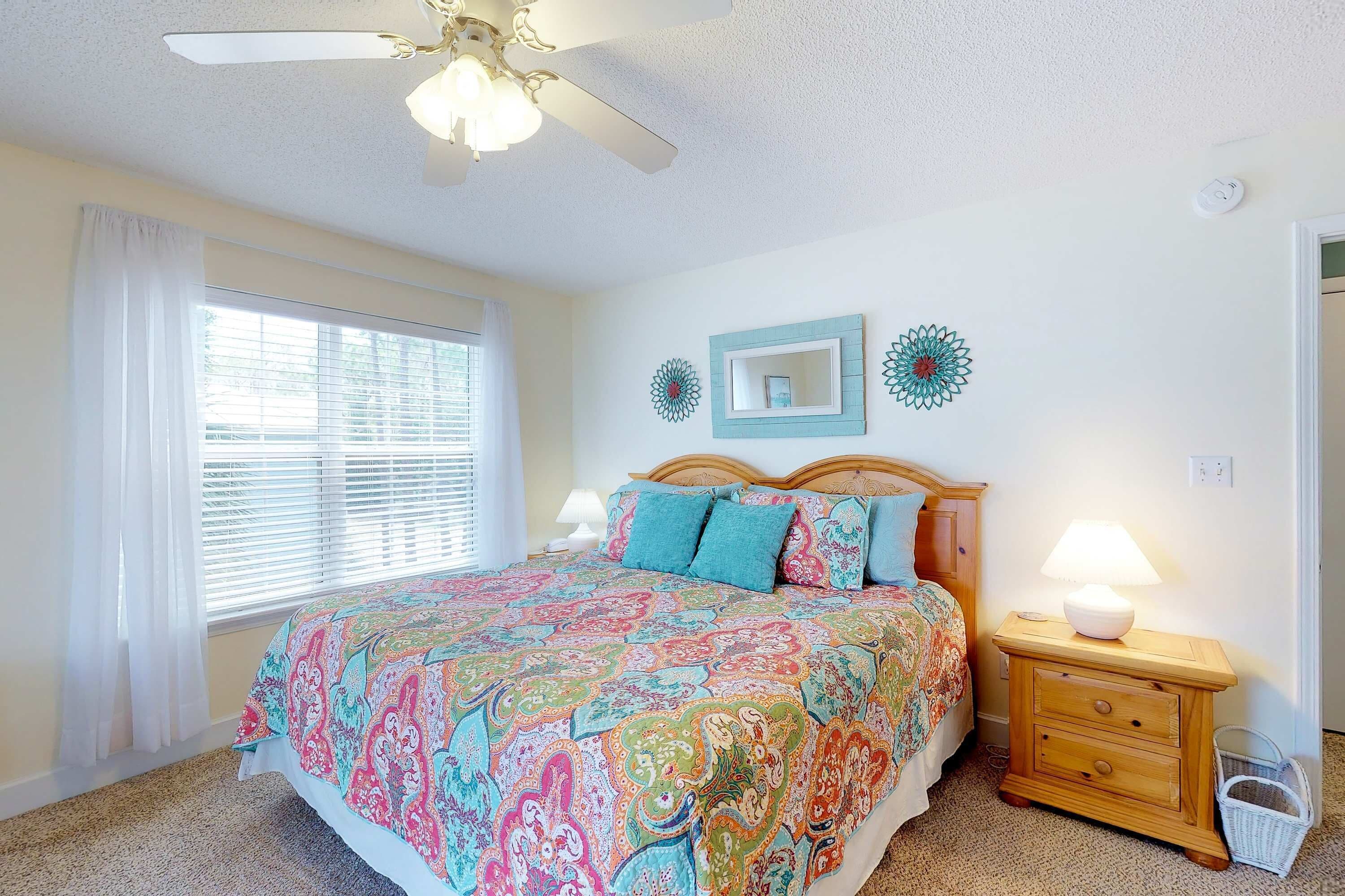 A bedroom with a bed, a nightstand, a ceiling fan, and a window with curtains.