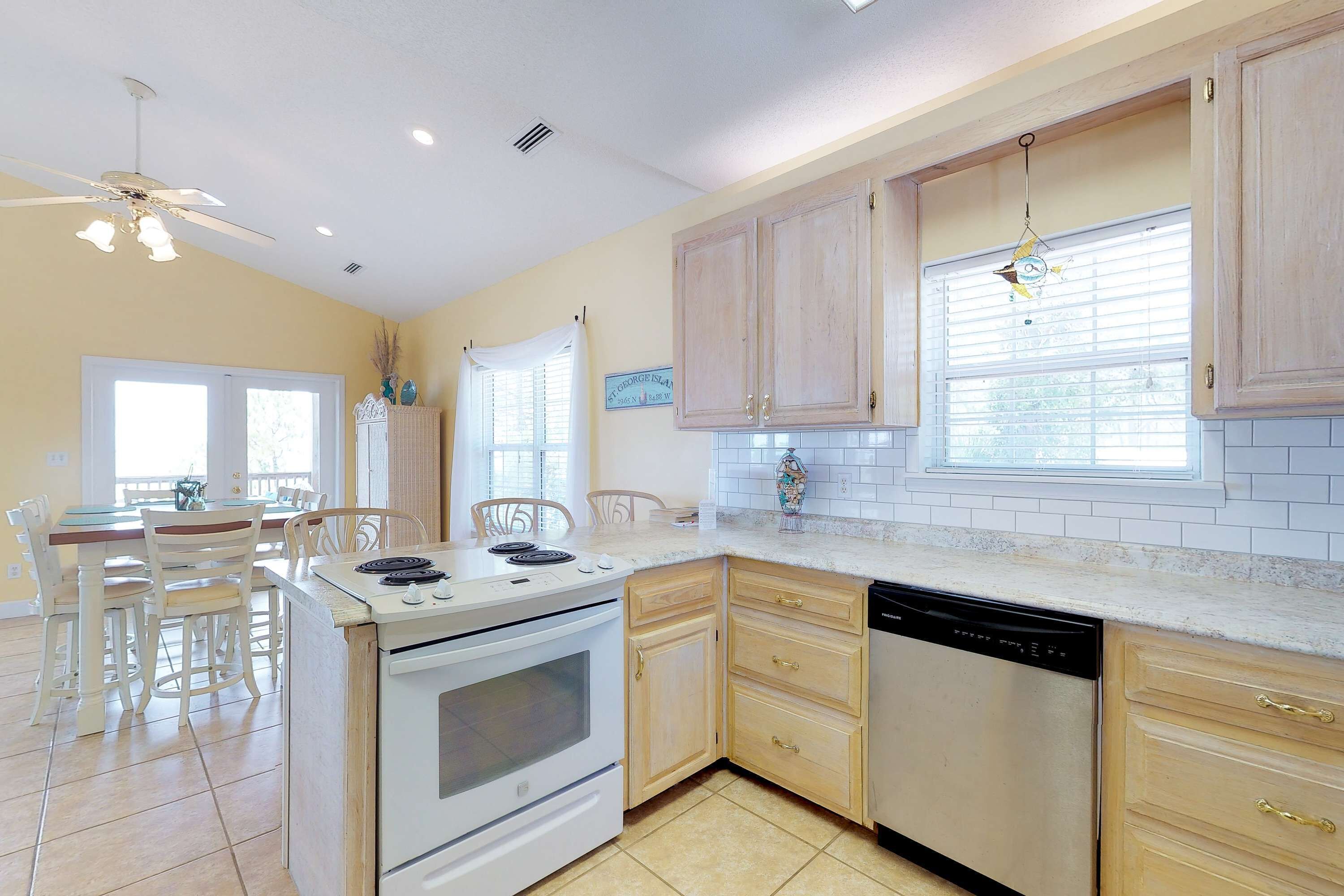 A kitchen with white cabinets, a stove, and a dishwasher. There is a dining area with chairs and a table.