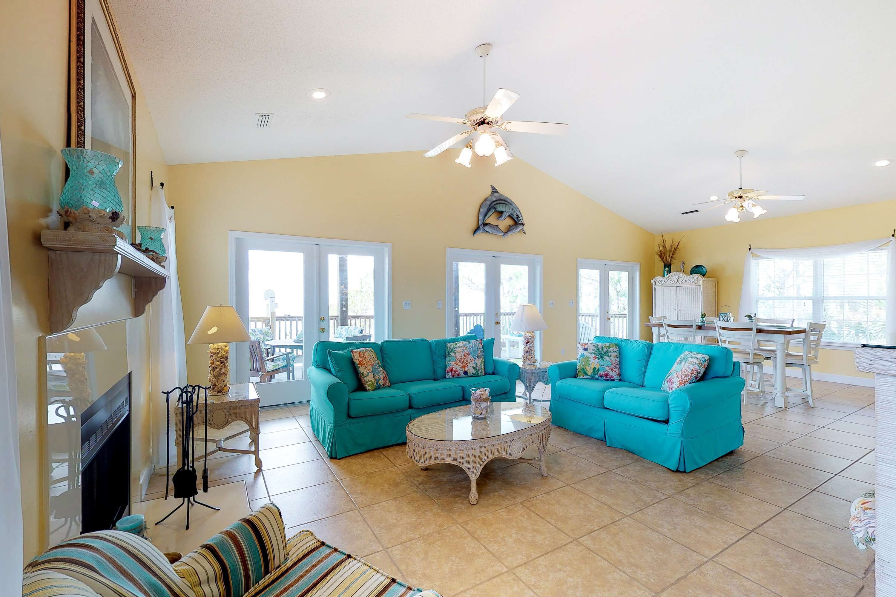 A spacious living room with two teal sofas, a round coffee table, and a ceiling fan.