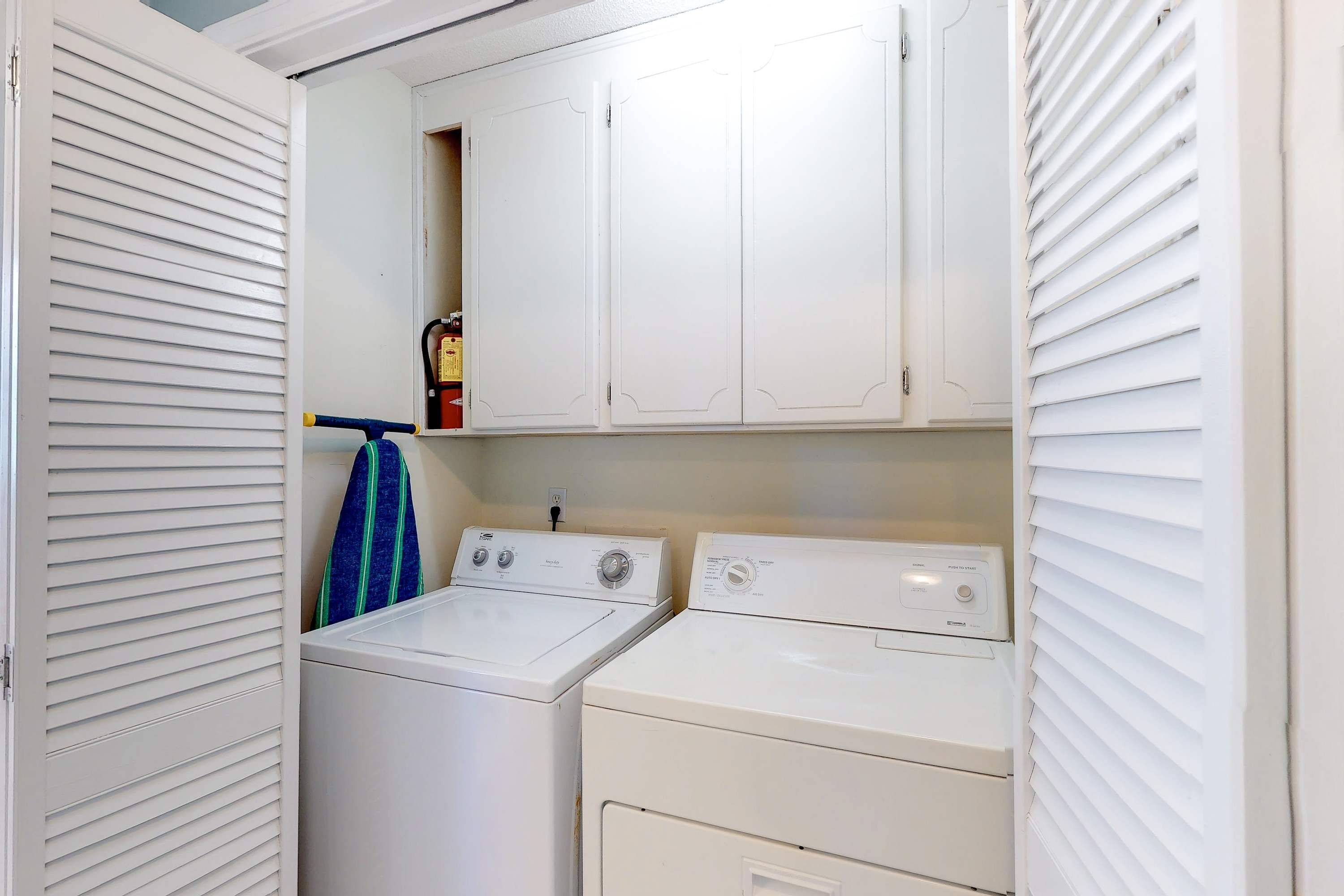A laundry room with two white washing machines, a drying rack, and a shelf with a bottle.