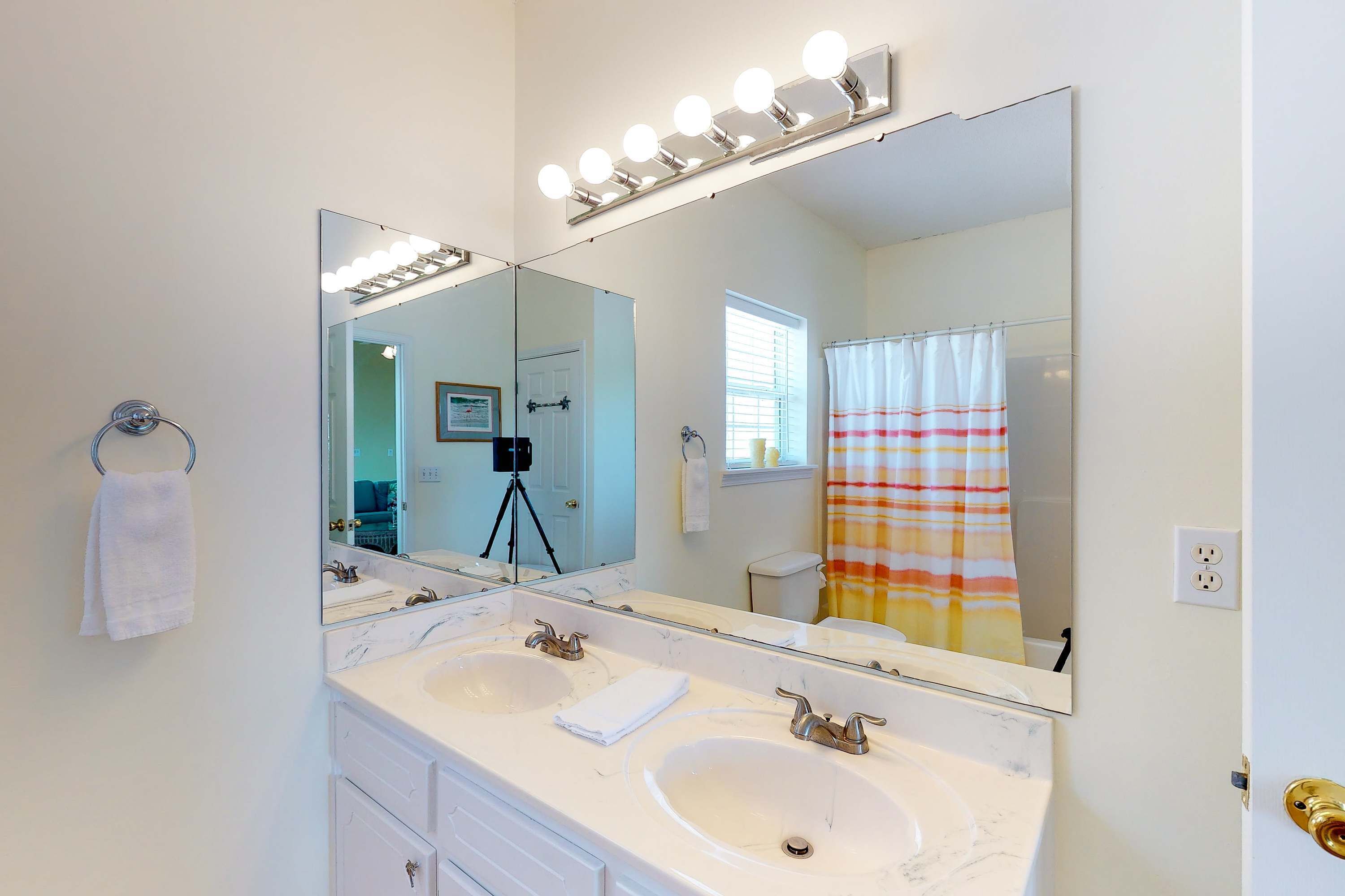Une salle de bain avec deux lavabos, un grand miroir avec éclairage, un porte-serviettes et un rideau de douche.