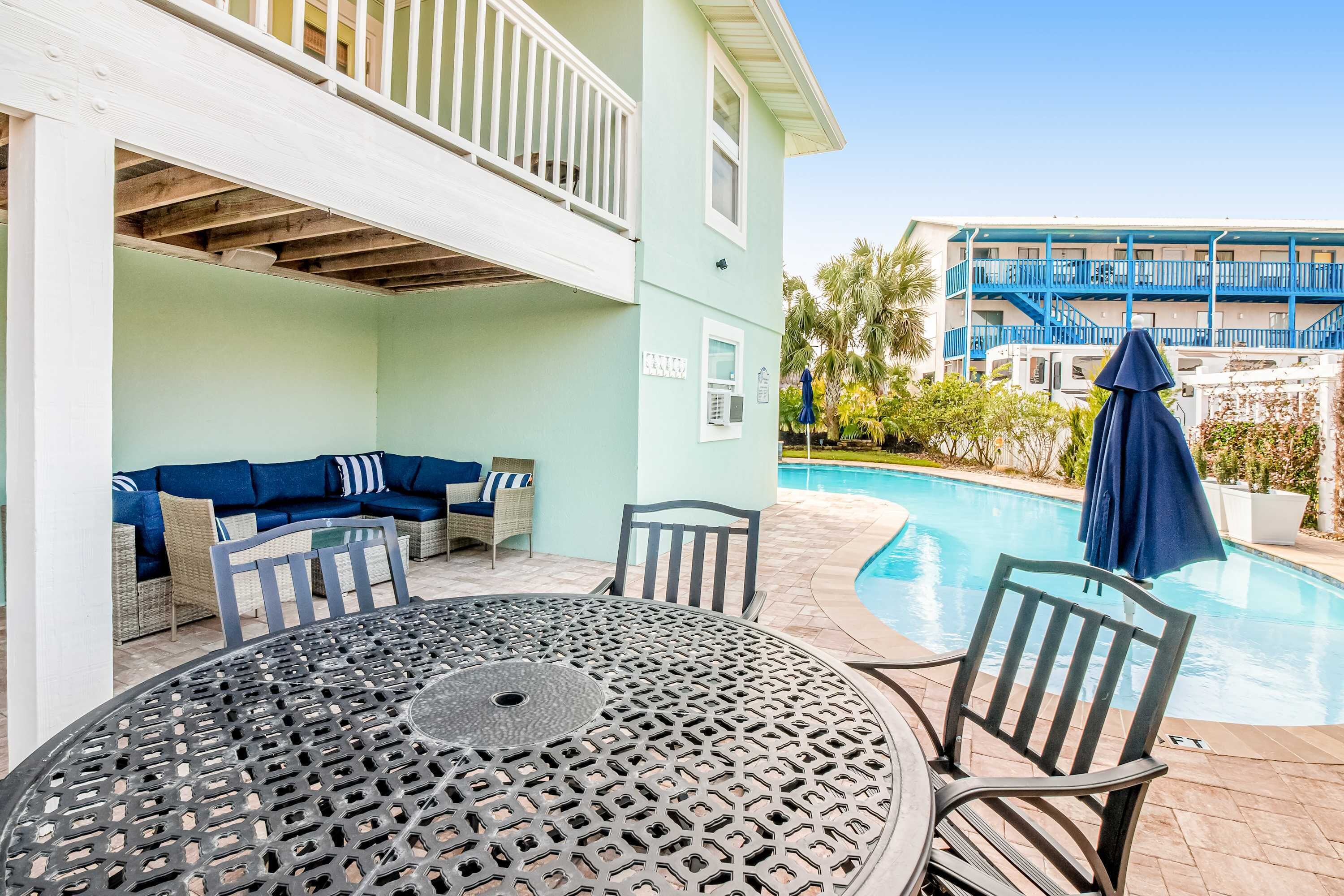 A poolside area with a round table and chairs, a sofa with cushions, and a pool.