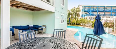 A poolside area with a round table and chairs, a sofa with cushions, and a pool.