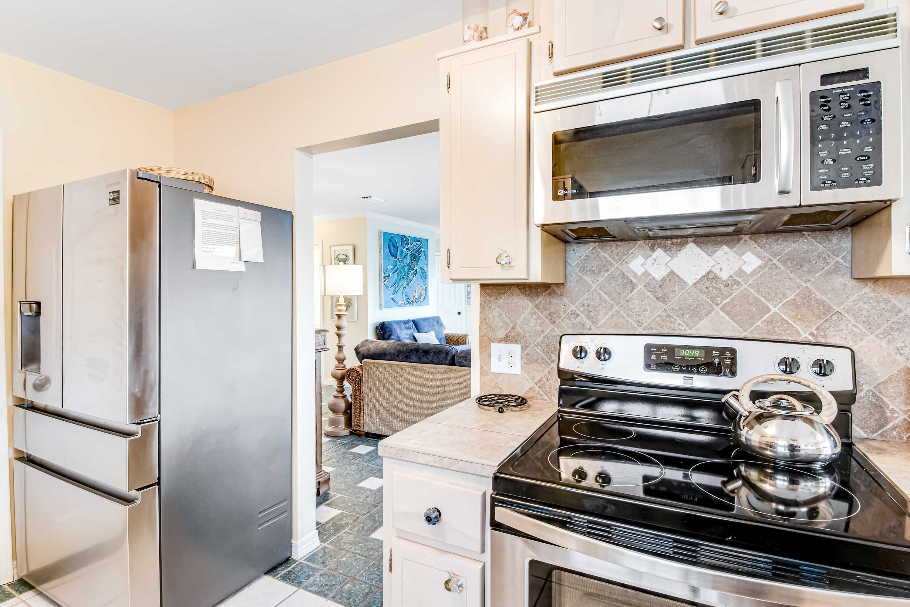 A kitchen with stainless steel appliances, a microwave, and a kettle on the stove.
