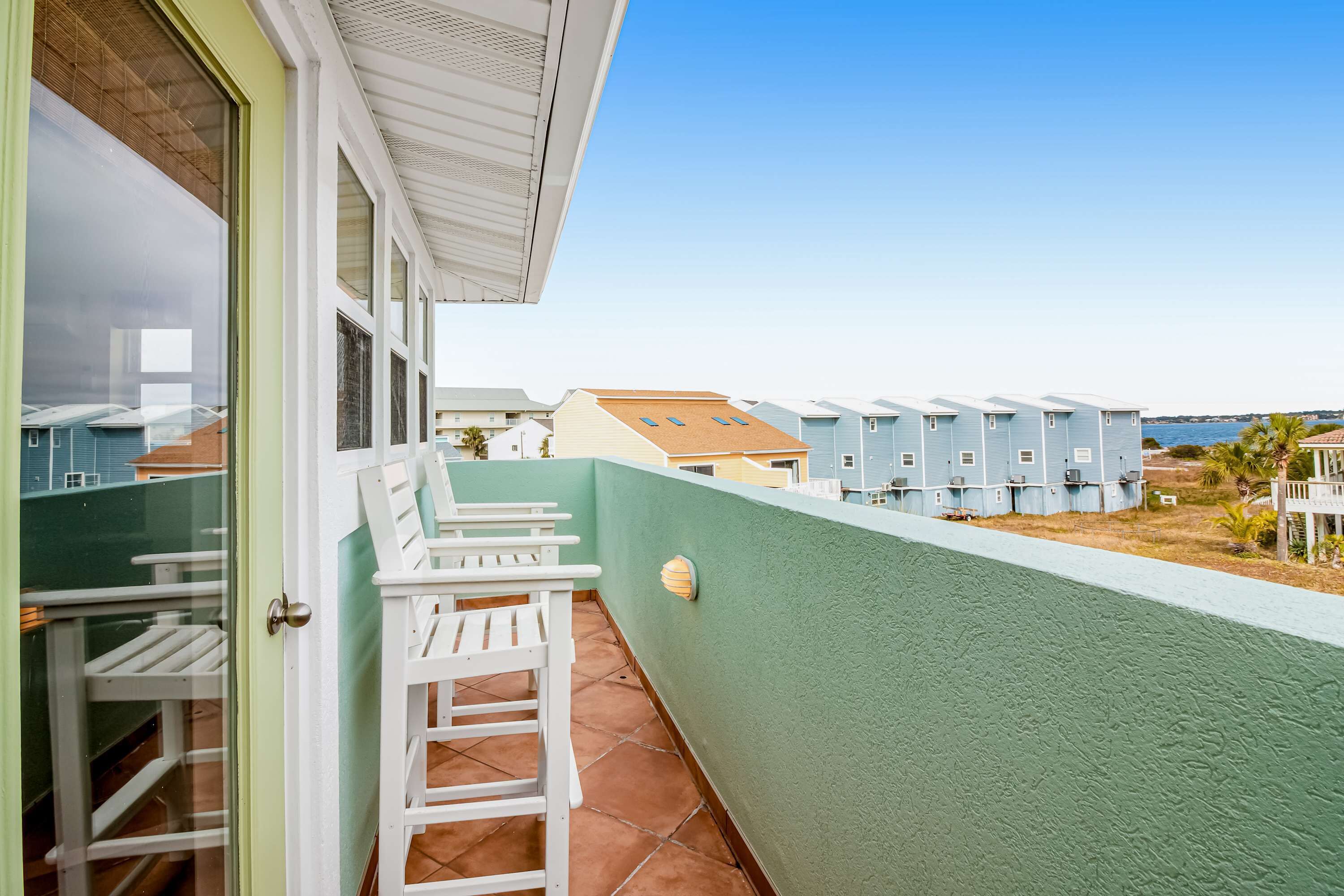 A balcony with white chairs, a green wall, and a view of other buildings.
