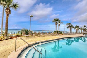 Zona junto a la piscina con sillones de descanso y palmeras, con vista a una playa.