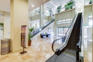 A spacious lobby with a central escalator, multiple levels, and potted plants. - Beachfront resort condo with gulf views, pools,splash pad, hot tub, & gym (Panama City Beach)