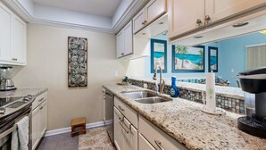 A kitchen with granite countertops, white cabinets, a sink, and a coffee maker. - Sound view townhome with balcony, alfresco dining, AC, & W&D - snowbird-friendly (Navarre)
