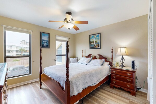 A bedroom with a four-poster bed, a ceiling fan, a nightstand with a lamp, and a window with a view of a vehicle outside. - Sound view townhome with balcony, alfresco dining, AC, & W&D - snowbird-friendly (Navarre)