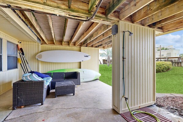 A covered outdoor area with a surfboard, wicker furniture, and a hose. - Sound view townhome with balcony, alfresco dining, AC, & W&D - snowbird-friendly (Navarre)