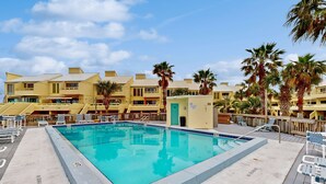 A swimming pool surrounded by palm trees and lounge chairs, with a building in the background. - Sound view townhome with balcony, alfresco dining, AC, & W&D - snowbird-friendly (Navarre)