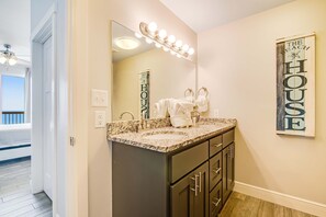 A bathroom with a vanity, double sink, and a large mirror with lights. There is a towel rack with towels and a sign on the wall that reads "The Beach House." - Beachfront resort condo with Gulf view, pools & gym - walk to Pier Park (Panama City Beach)