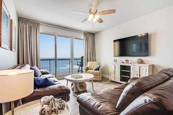 A living room with a sofa, a coffee table, a TV, and a balcony with a view. - Beachfront resort condo with Gulf view, pools & gym - walk to Pier Park (Panama City Beach)