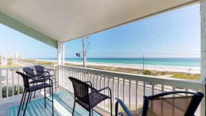 Uma varanda com duas cadeiras e uma mesa, com vista para uma praia de águas azuis cristalinas e areal dourado.
