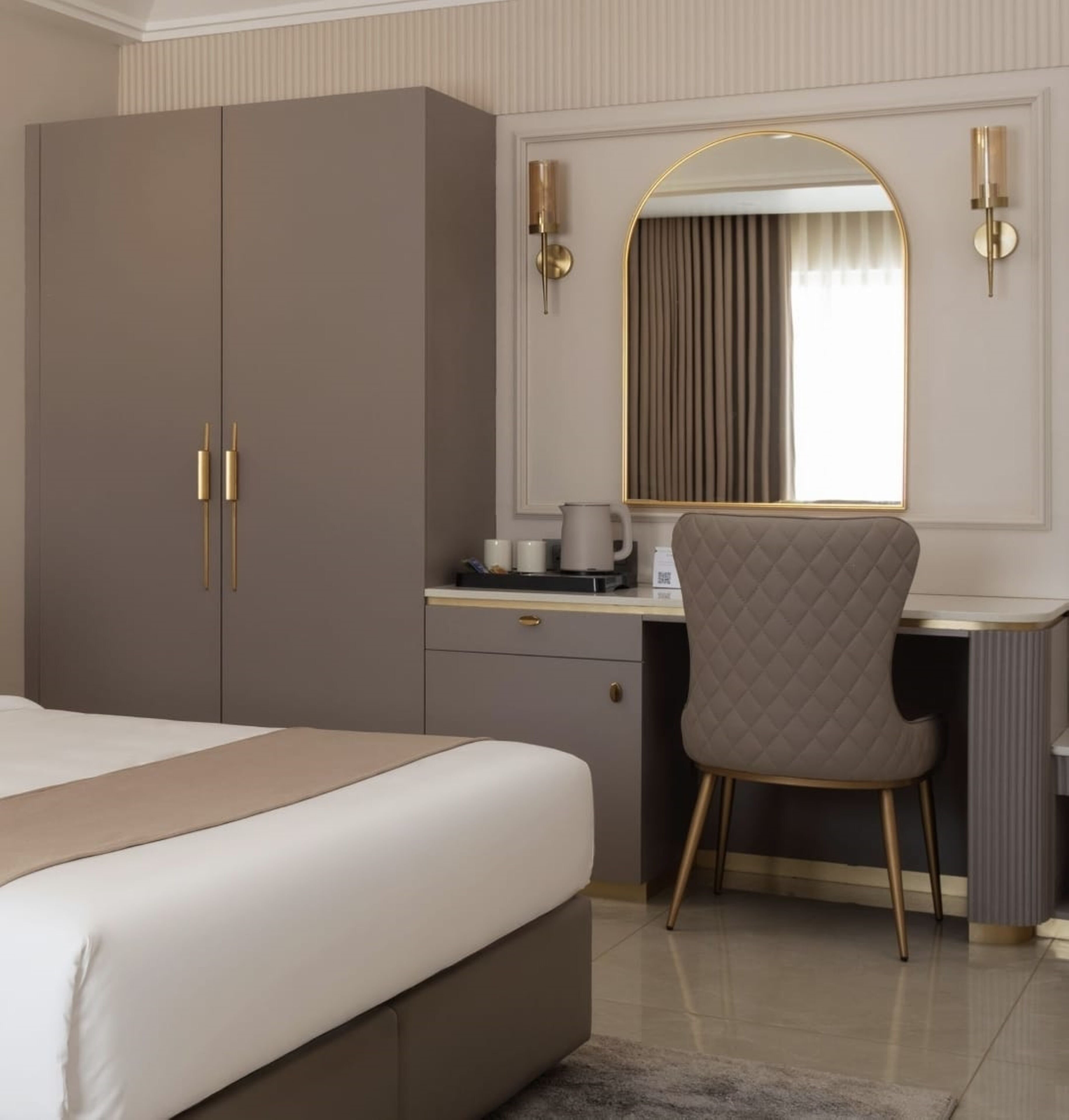 A hotel room with a bed, a desk, a chair, and a large mirror.