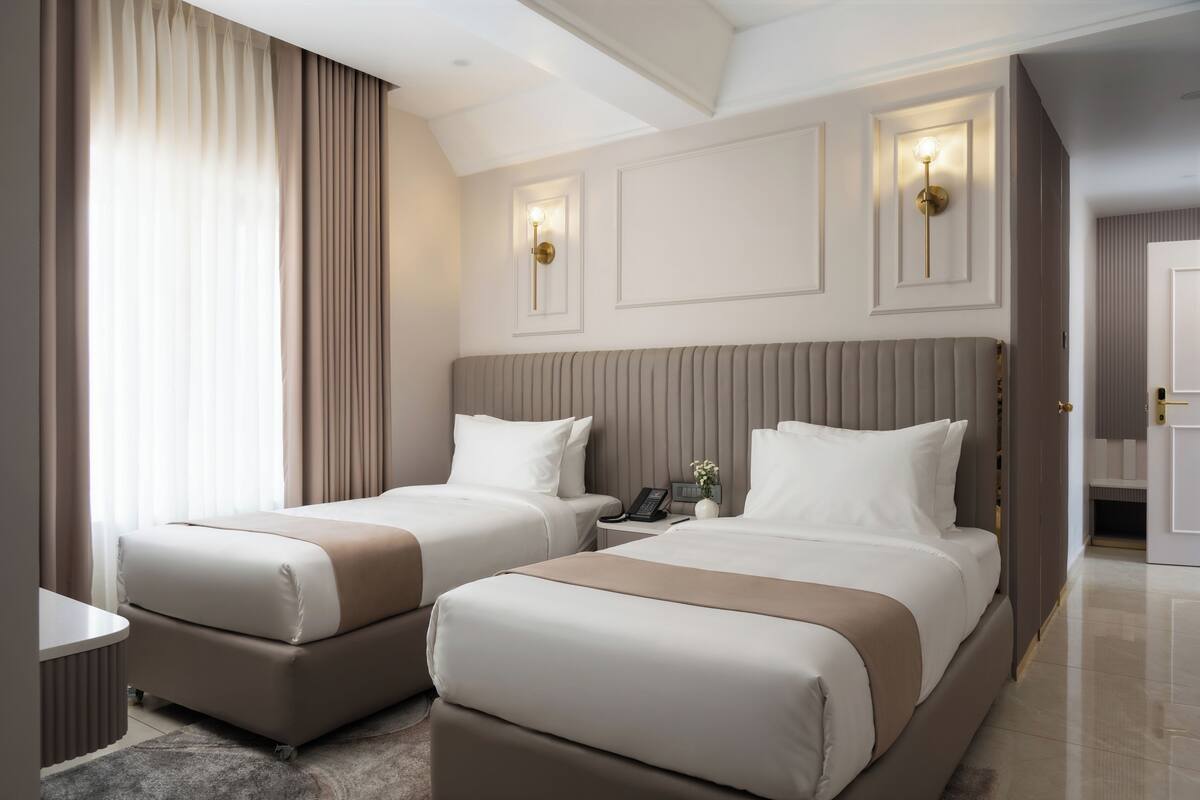 Une chambre d’hôtel avec deux lits, une table de chevet, une lampe et une vue sur le couloir.