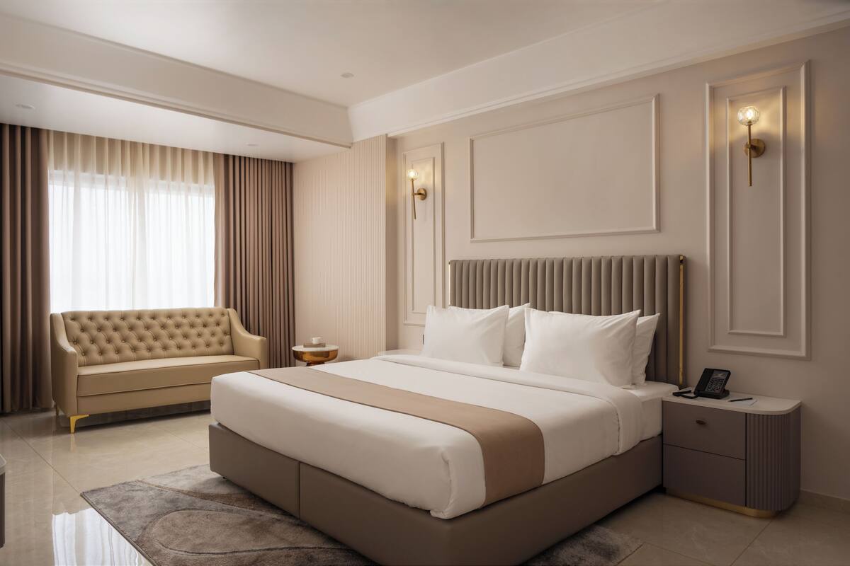 Une chambre moderne avec un grand lit, un canapé, une table de chevet et un luminaire fixé au mur.