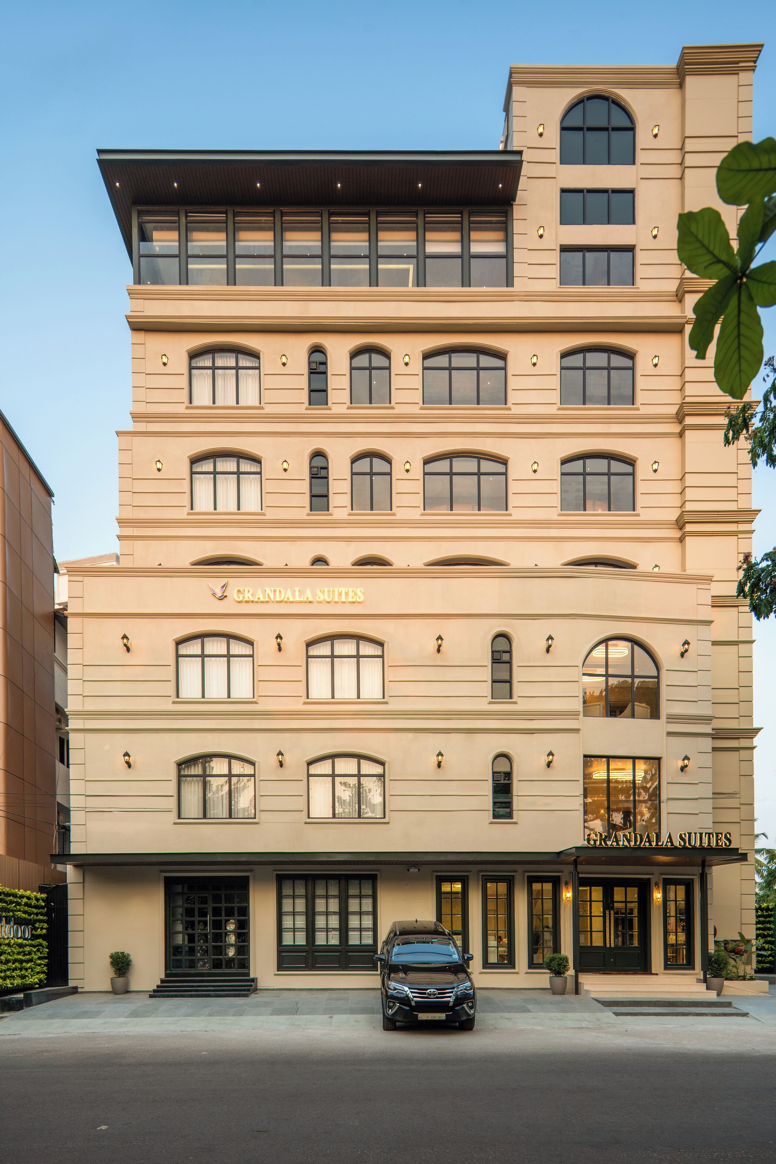 A multi-story hotel with a classic architectural design, featuring a prominent entrance and a car parked in front.