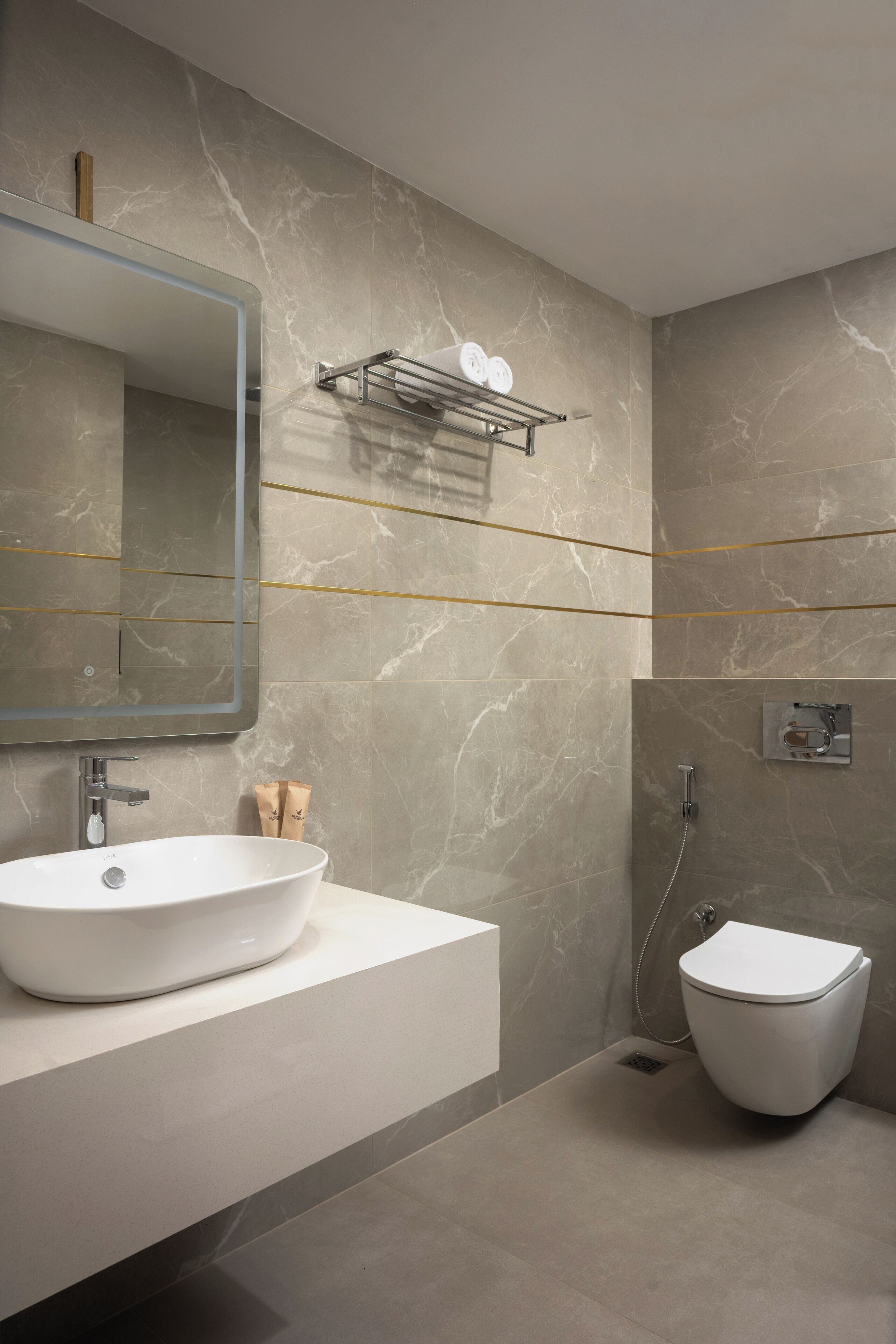 A modern bathroom with a large mirror, a white sink, a toilet, and a towel rack.