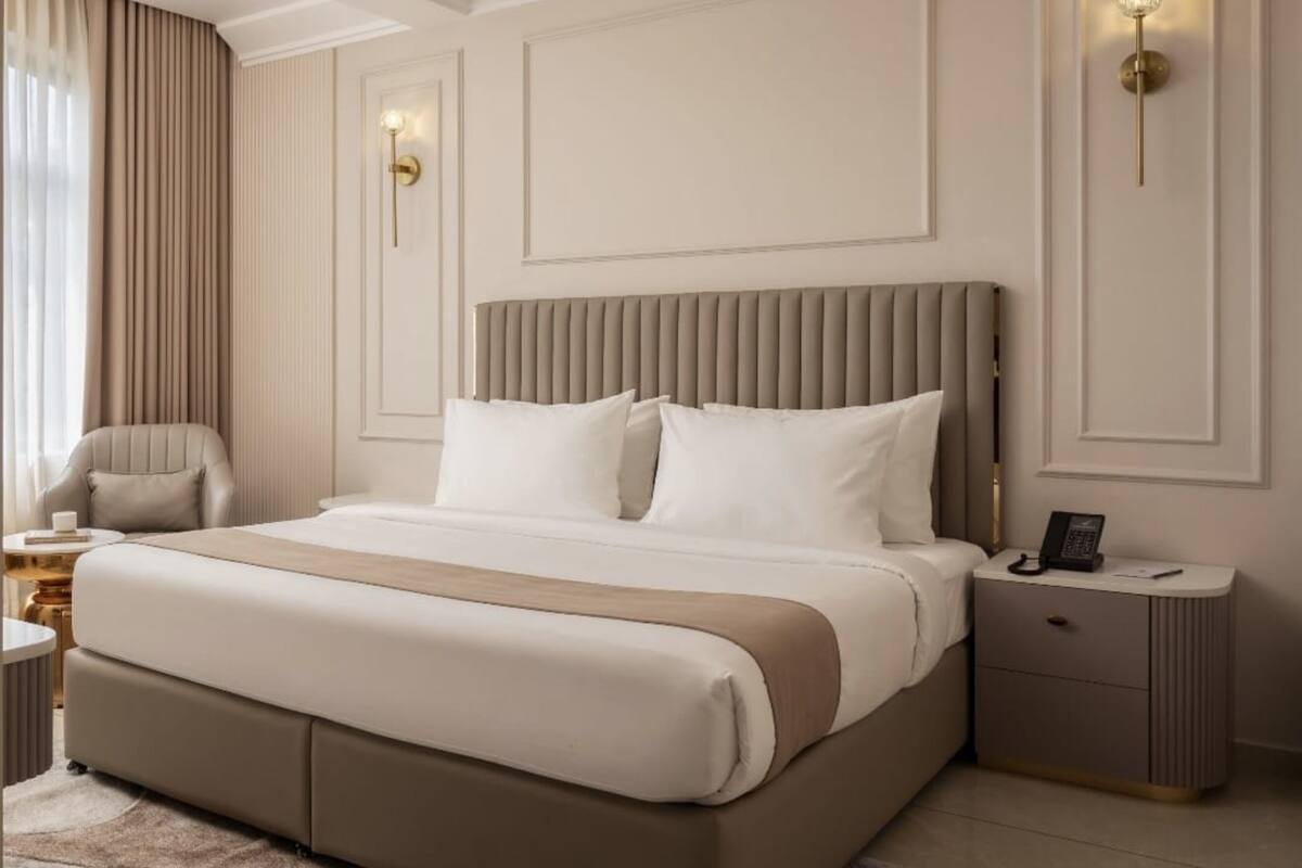 Une chambre d’hôtel moderne, dotée d’un grand lit, d’une table de chevet, d’une chaise et d’un luminaire fixé au mur.