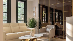 Ein modernes Wohnzimmer mit einem beigen Sofa, einem weißen Sessel, einem runden Couchtisch mit goldener Basis und einer großen Chandelier.