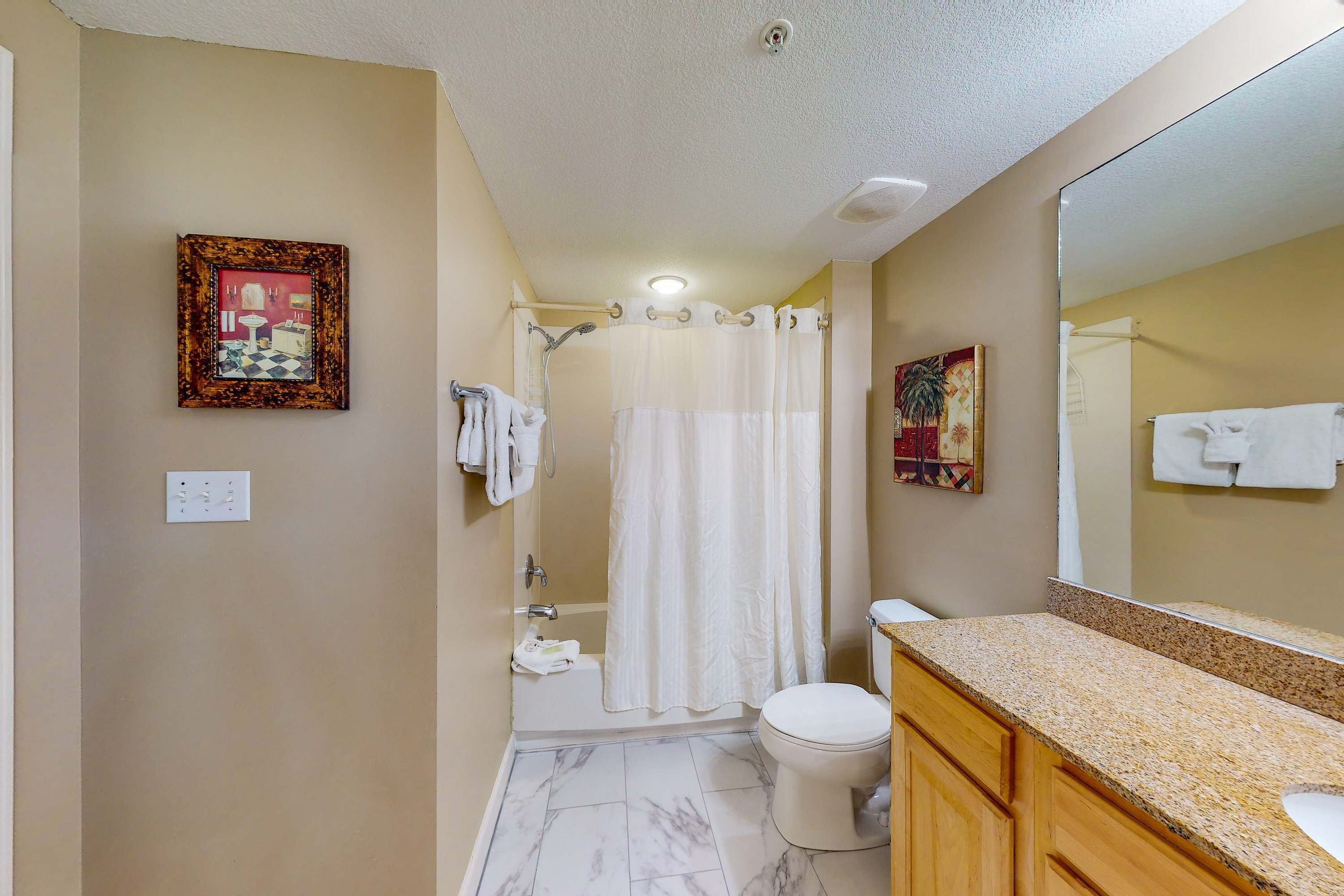 Une salle de bain avec une douche, des toilettes et un lavabo. Un tableau encadré est accroché au mur, et un miroir se trouve au-dessus du lavabo.