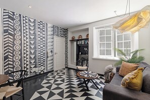 Un salon moderne avec un sol à motifs géométriques, un canapé avec des coussins, une table ronde et une chaise.