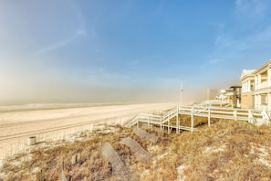 Un hôtel situé en bord de mer, avec un escalier menant à la plage, entouré d’herbes sèches et de dunes.
