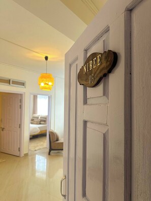 A room with a wooden door labeled "NIREE 06" and a bed with a white and gray striped blanket.