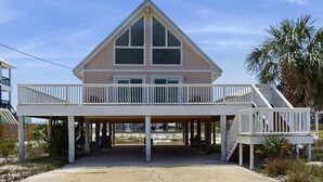 Een huis aan het strand met een balkon, een overdekte entree en een palmboom.