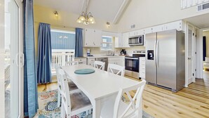 Een moderne keuken met witte kasten, roestvrijstalen apparatuur en een eethoek met een witte tafel en stoelen.