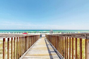 A wooden boardwalk leading to a beach with umbrellas and people in the distance. - Beachfront condo with pool, tennis, fitness center & WiFi (Navarre Beach)