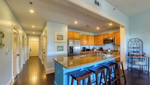 Eine moderne Küche mit Holzschränken, einem Edelstahlkühlschrank, einer Mikrowelle und einer großen Kochinsel mit Barhocker.