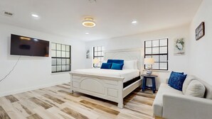Un dormitorio con una cama blanca, un televisor y un sofá.