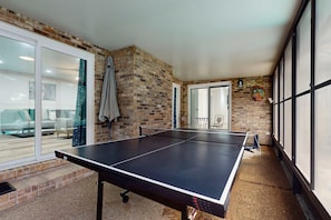 Ein Tischtennistisch in einem Raum mit Ziegelwänden, großen Fenstern und einer Glastür, die auf einen Balkon führt.