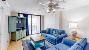 Ein Wohnzimmer mit einem blauen Sofa, einem Holztisch, einer grünen Unterhaltungseinheit und einem Deckenventilator.
