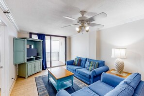Un soggiorno con un divano blu, un tavolino in legno, un mobile TV verde e una ventola a soffitto.