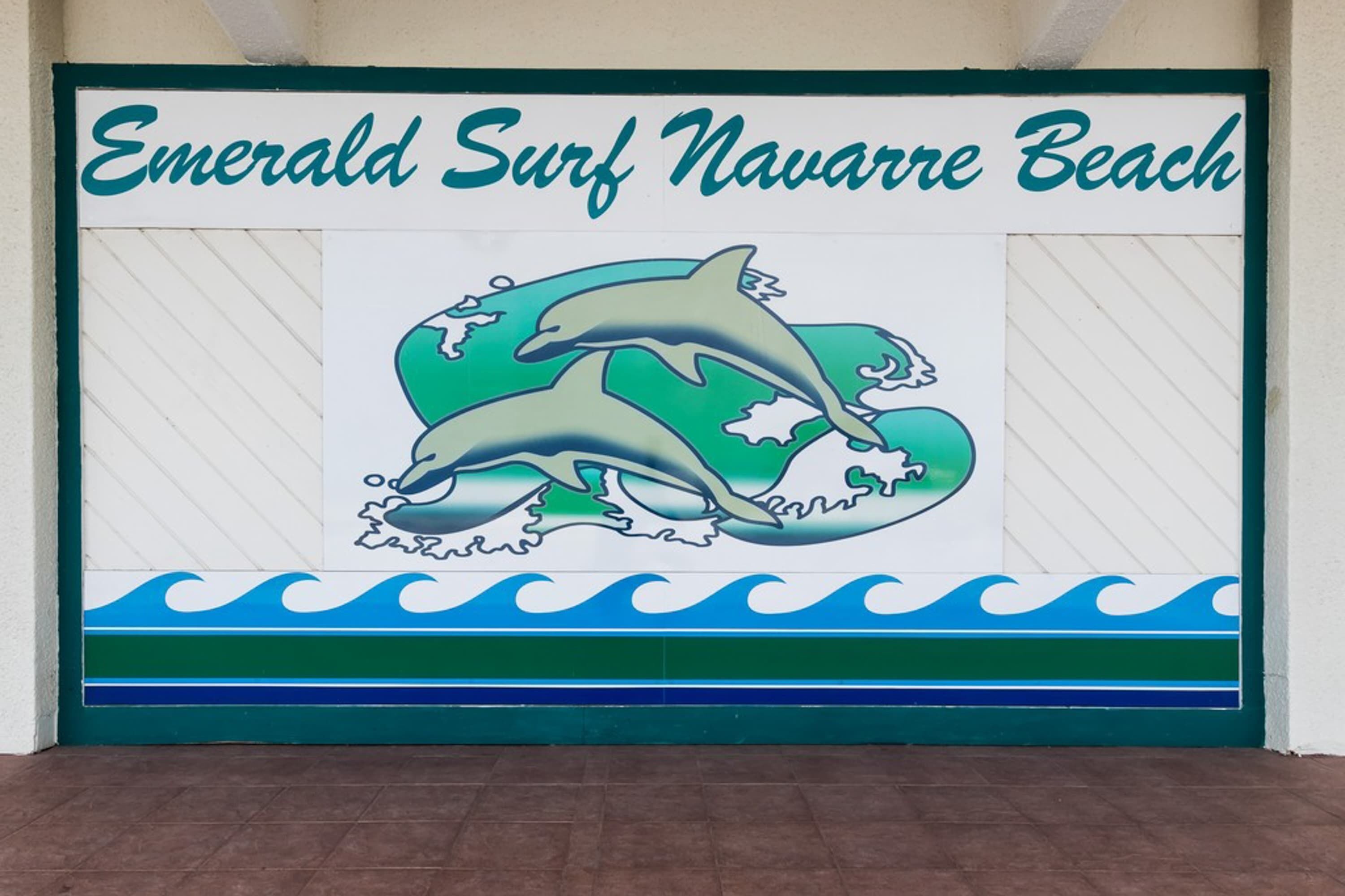 Schild für Emerald Surf Navarre Beach mit Delphinen und Wellen.