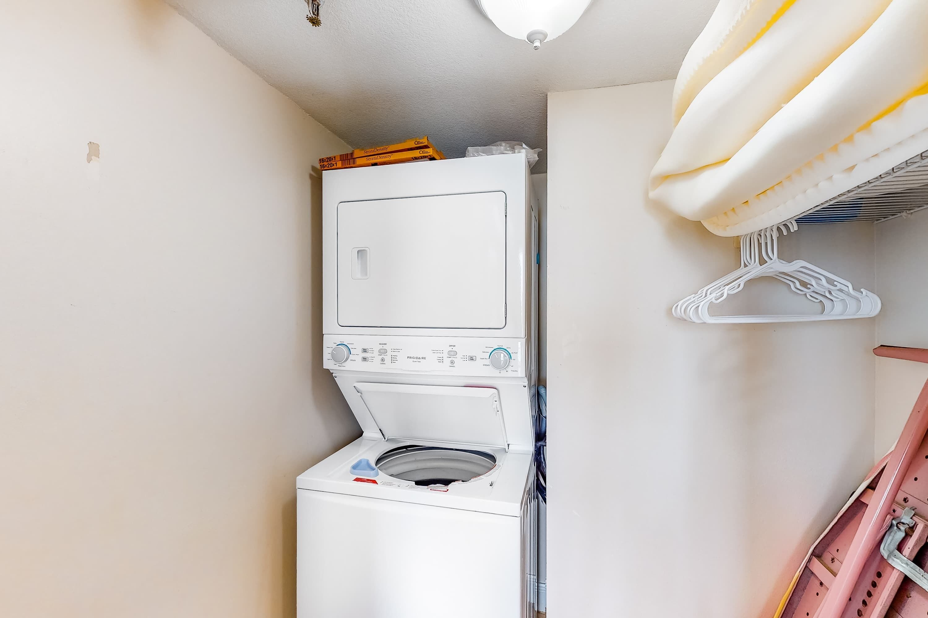 Een kleine wasruimte met een voorlader wasmachine, een droogrek en een klein rek met opgevouwen kleding.